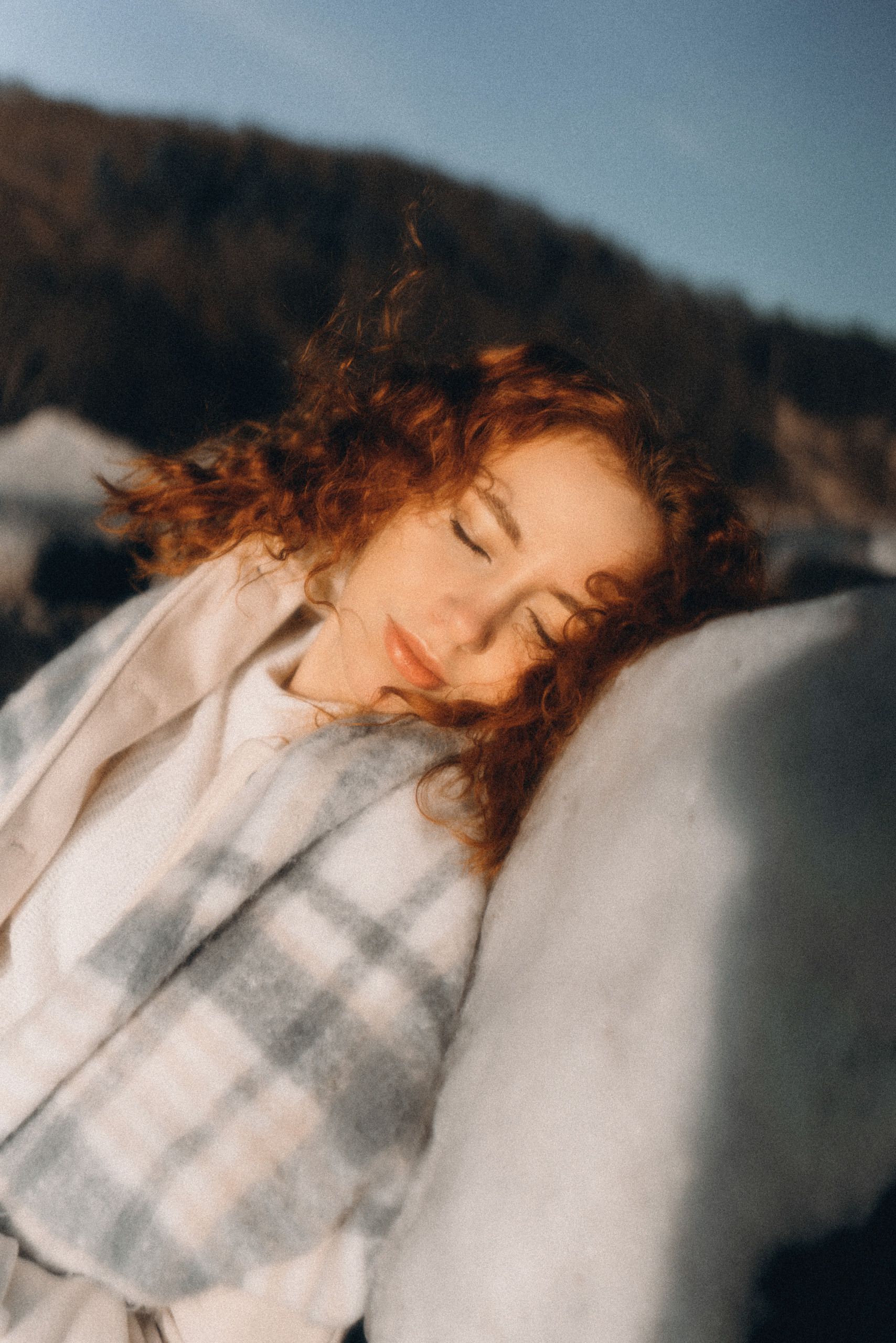 A serene woman with auburn hair resting on a rock in a winter landscape.