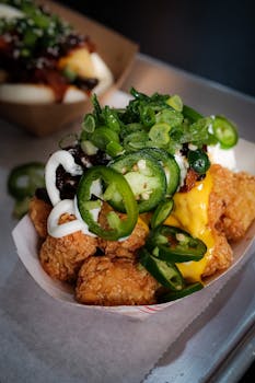 Close-up image of loaded tater tots with toppings like jalapeños, cheese sauce, and scallions.