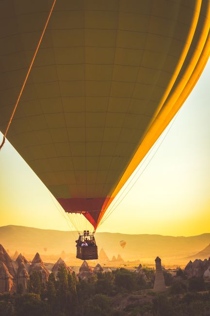 A hot air balloon soars over Cappadocia's unique rock formations at sunset, creating a picturesque travel scene.