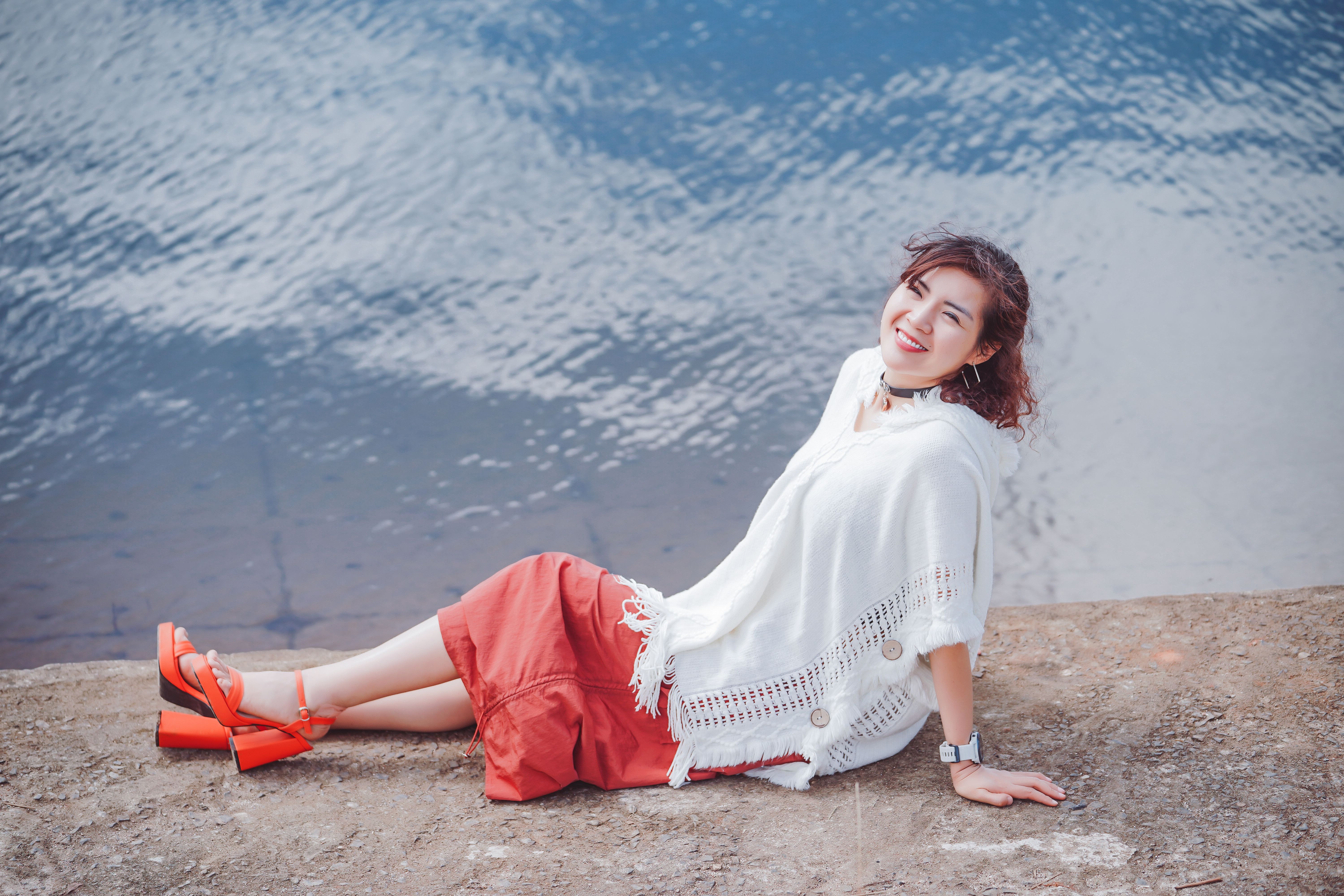 A cheerful woman in a red skirt sits by the water, enjoying a peaceful day.