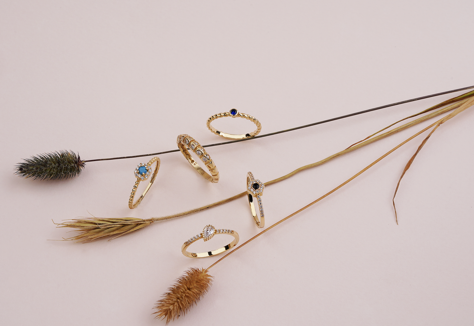 styled flat-lay of alternative gemstone engagement rings showing a blue sapphire, pink morganite, and salt-and-pepper diamond in rose gold settings on a soft linen surface