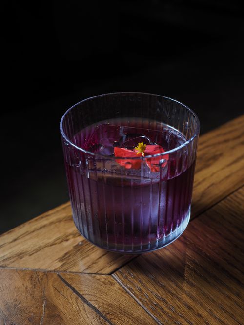 Free A close-up shot of an elegant purple cocktail in a textured glass, adorned with a red and yellow flower. Stock Photo