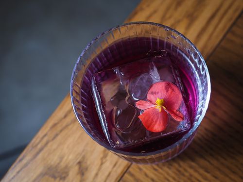 Free Close-up of a purple cocktail with an ice cube and flower, perfect for bar menus. Stock Photo