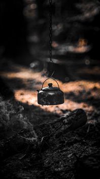 Moody forest setting with a hanging kettle and burning embers. Perfect camping ambiance.
