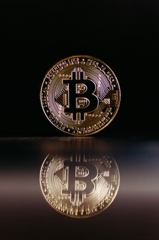 Close-up of a golden Bitcoin coin reflecting on a dark surface, symbolizing digital currency.