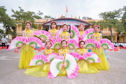 A vibrant group of young women in traditional Vietnamese dress performing a cultural fan dance outdoors.