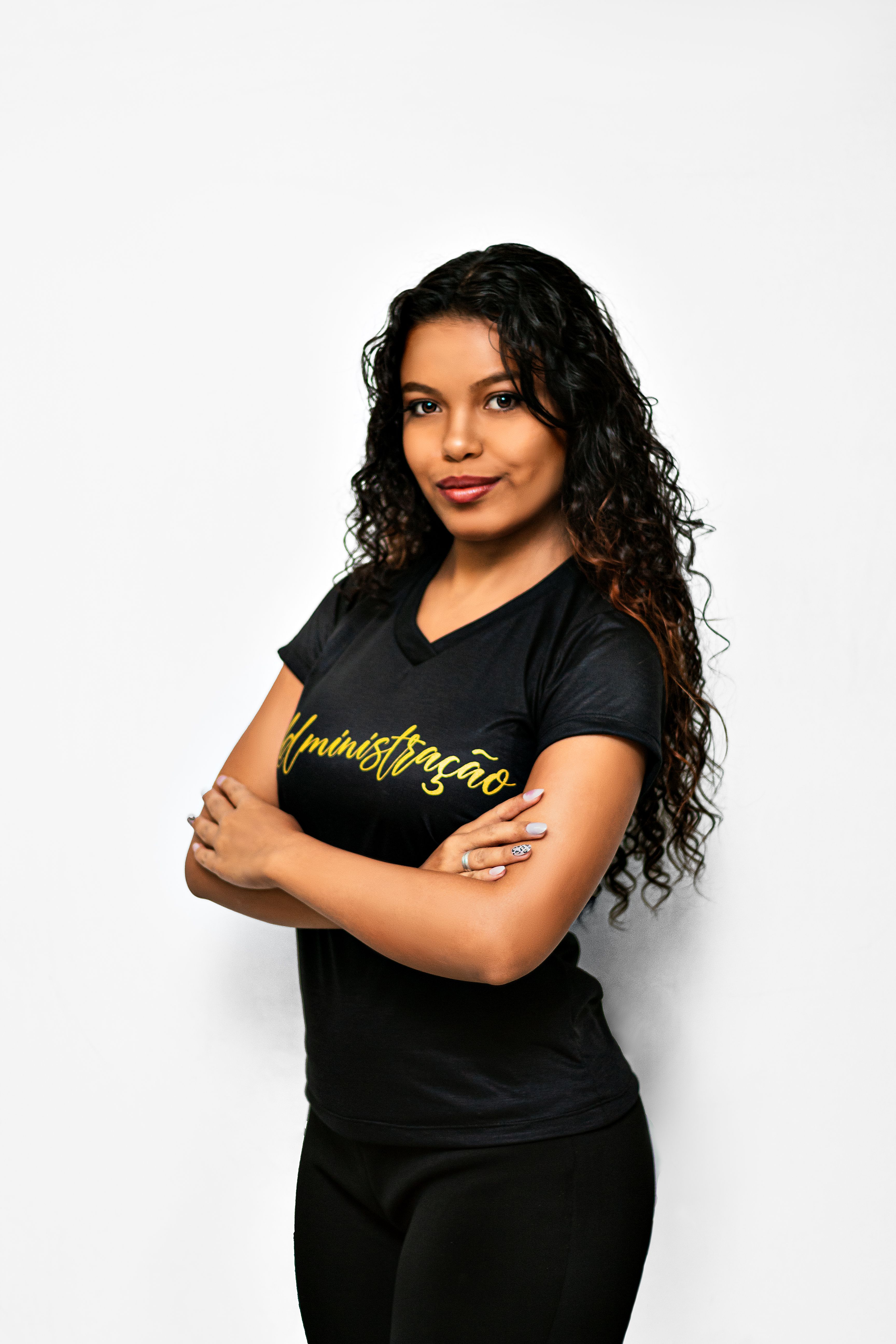 Studio portrait of a confident woman with curly hair and red lips, posing with arms crossed.