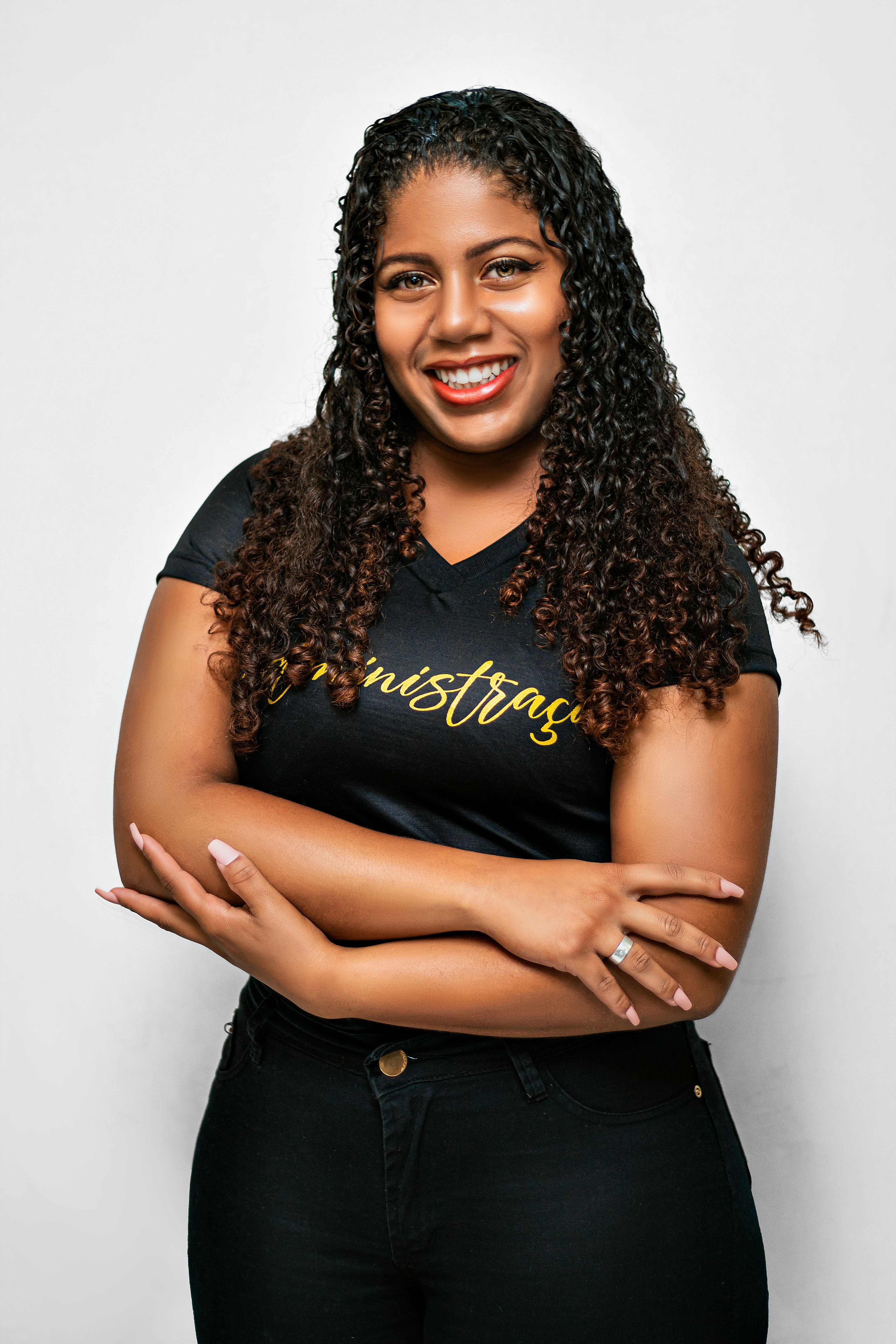 Portrait of a confident woman with curly hair smiling and crossing her arms in a studio setting.