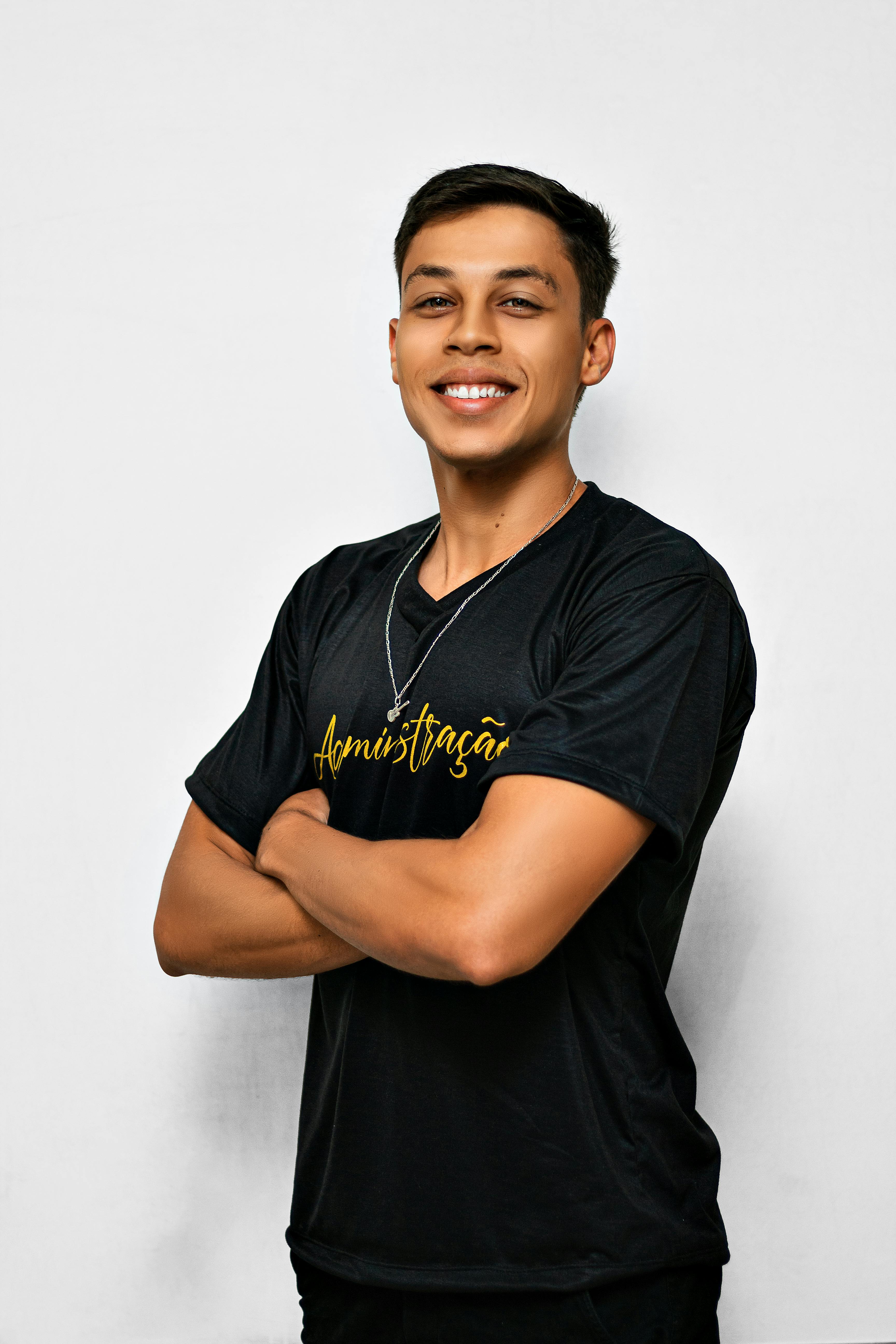 Portrait of a young man smiling confidently with arms crossed in a studio setting.