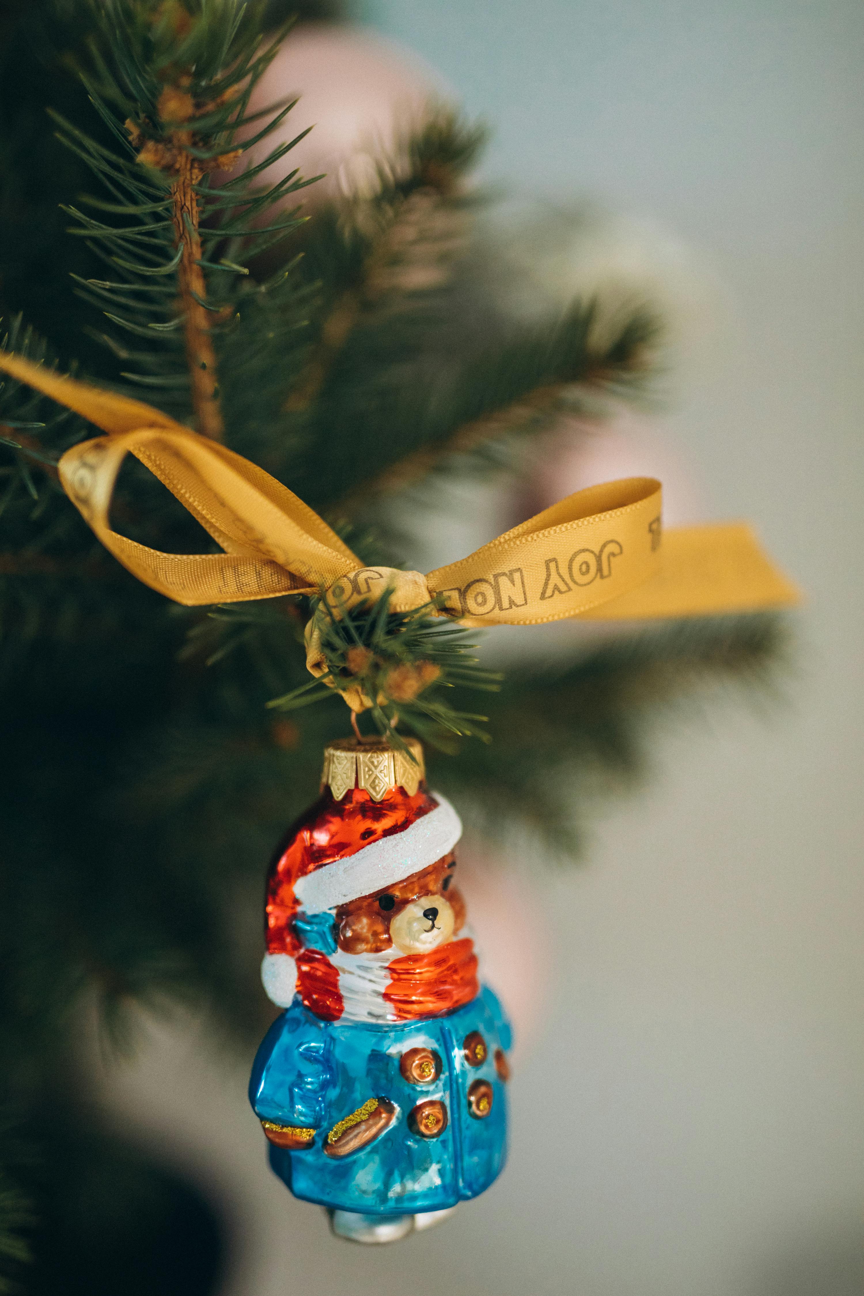 Close-up of a teddy bear ornament with ribbon on a Christmas tree branch.