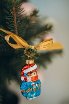 Close-up of a teddy bear ornament with ribbon on a Christmas tree branch.