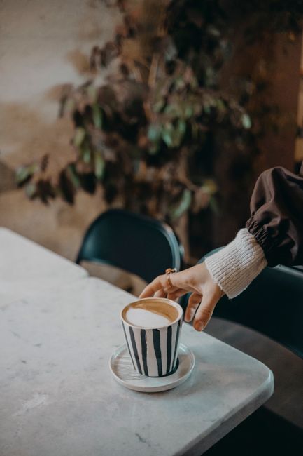 A hand reaching for a striped coffee cup on a marble table, creating a cozy atmosphere.