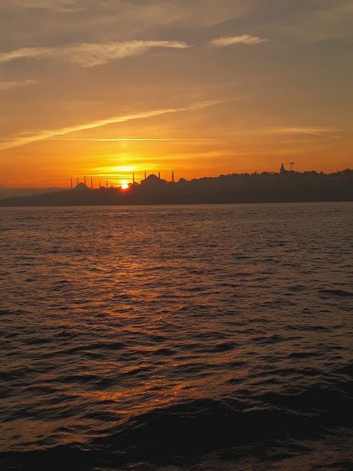 Free Stunning sunset view over the water with Istanbul's historic skyline silhouetted against the vibrant sky. Stock Photo