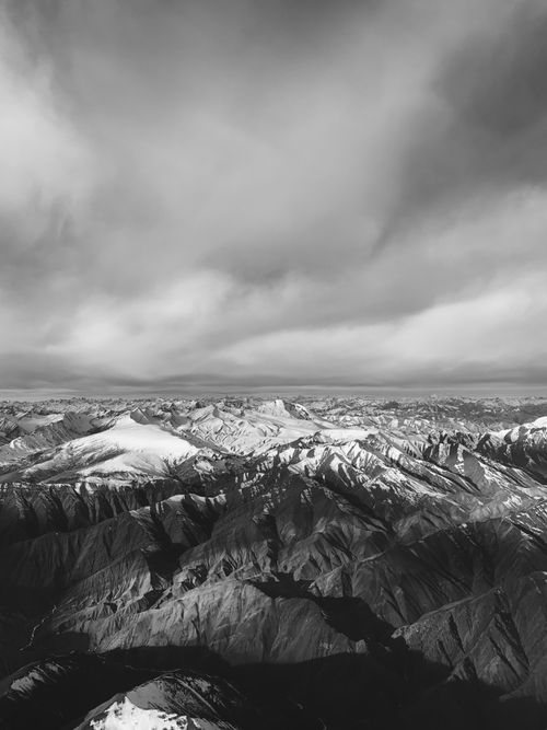 Free Dramatic black and white aerial shot of a vast, snowy mountain range with an overcast sky. Stock Photo