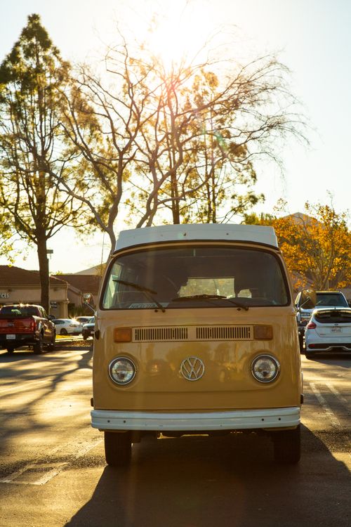 Free Classic Volkswagen Type 2 van parked in a sunlit parking lot with autumn trees in the background. Stock Photo