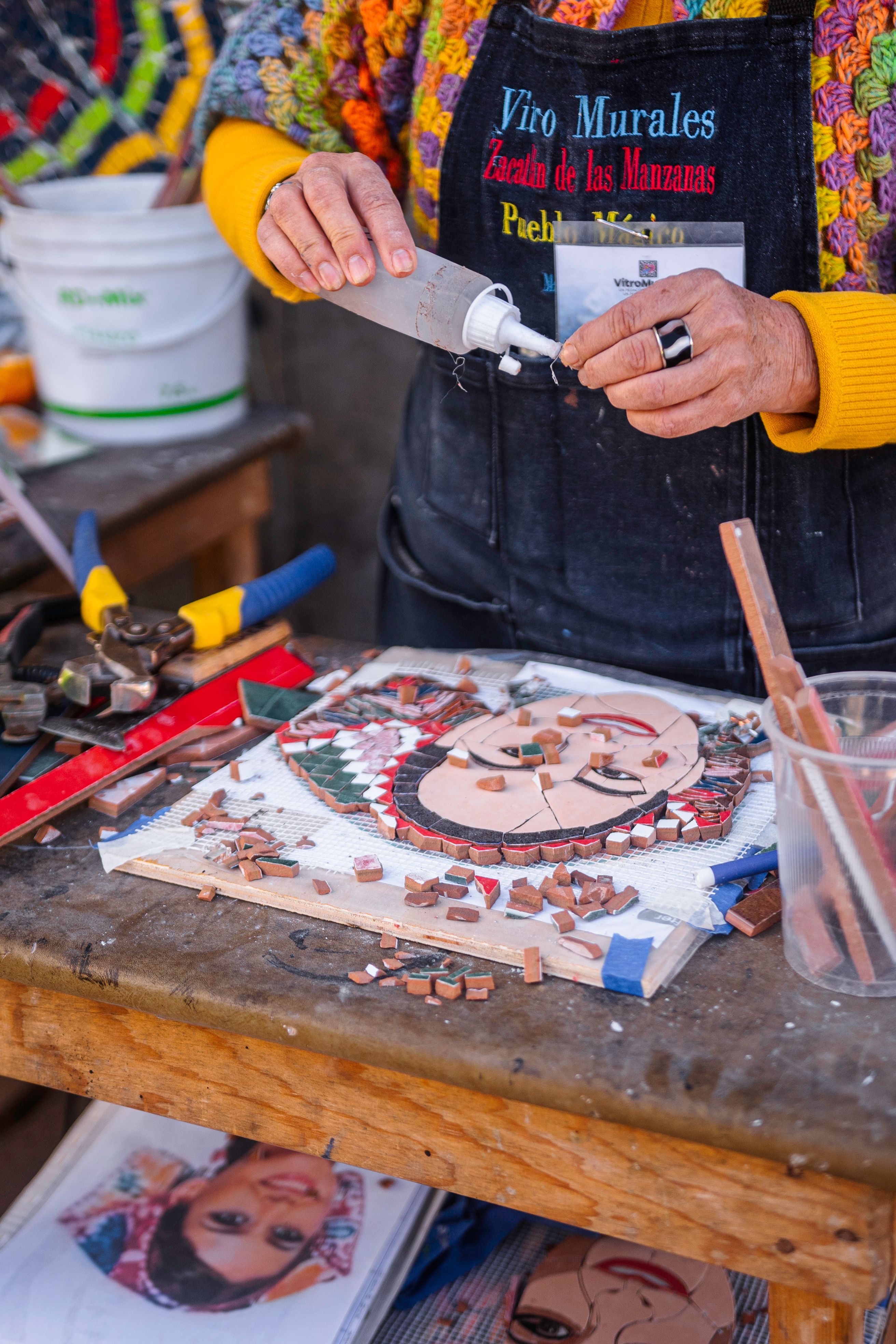 A well-organized craft table with various colors of junk mail sorted into containers, along with scissors, glue, and a base for the mosaic.