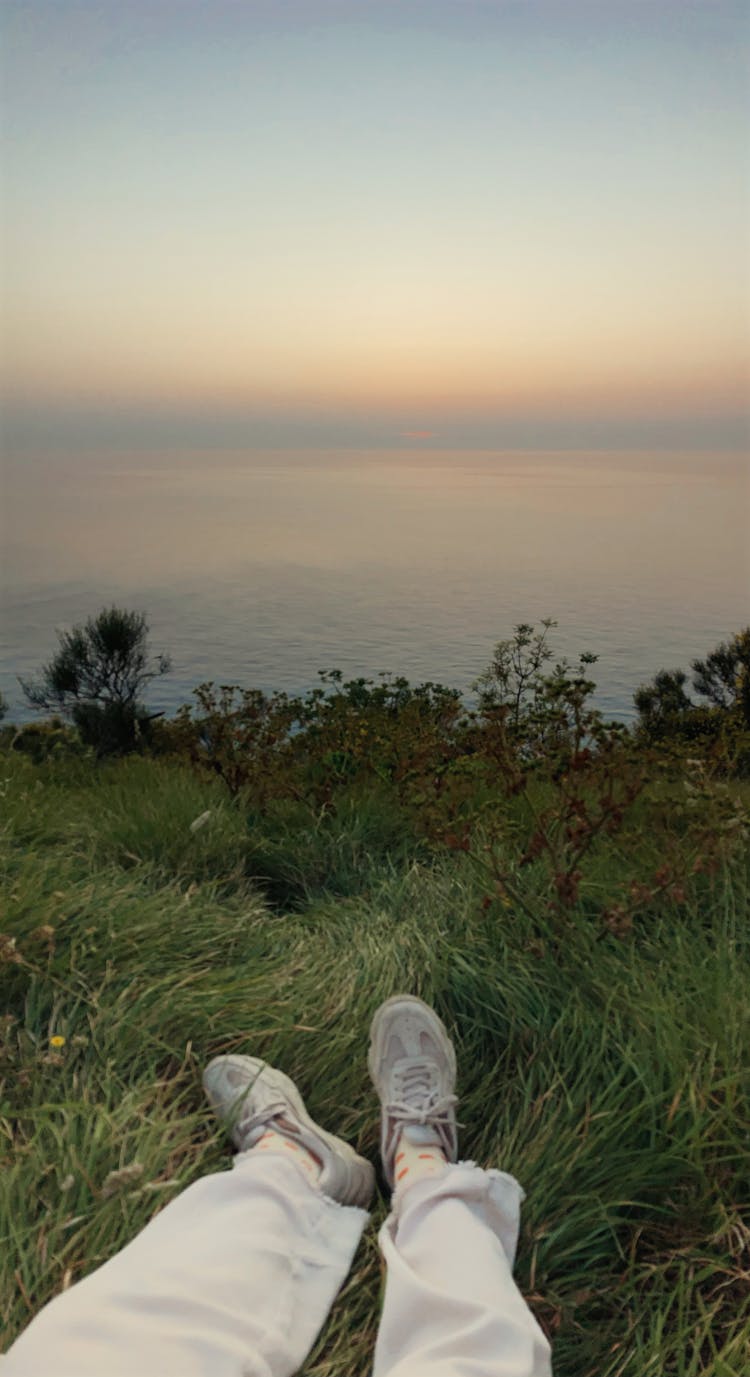 Person Legs In Grass At River Bank On Sunset