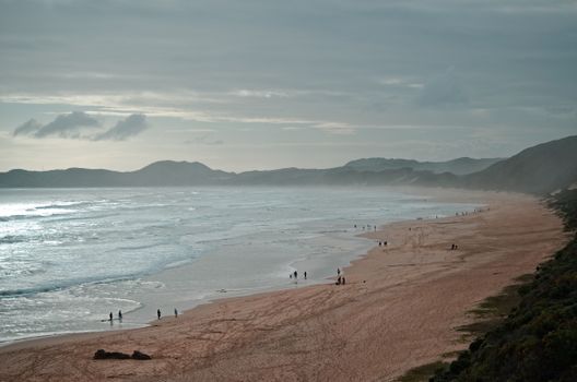 Tranquil beach scene with gentle waves and people strolling in serene evening light.