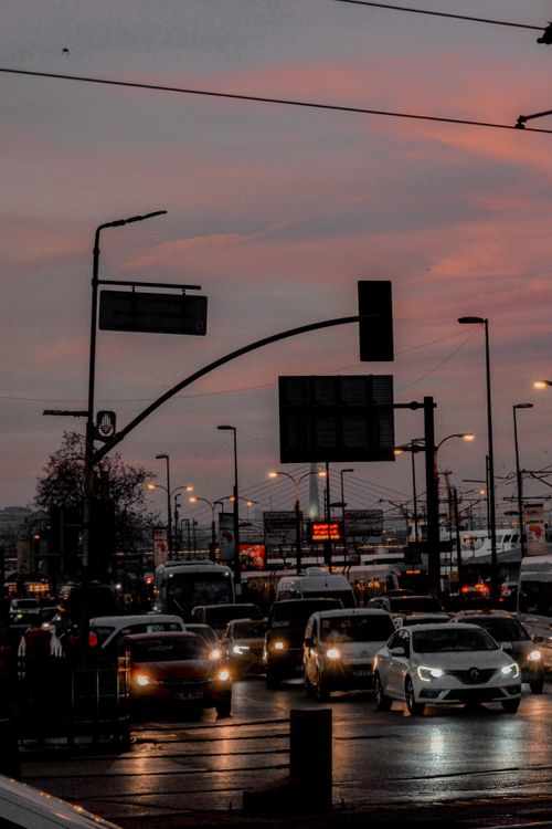 Free A city street bustling with traffic under an overcast dusk sky, reflecting wet roadway surfaces. Stock Photo