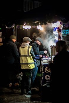 People enjoying a warm beverage at a cozy winter night market stall.