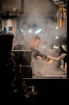 A female chef skillfully cooking in a smoky kitchen, creating a vibrant culinary scene.