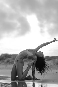 Dynamic yoga pose on a beach captured in black and white at sunrise, highlighting flexibility and grace.