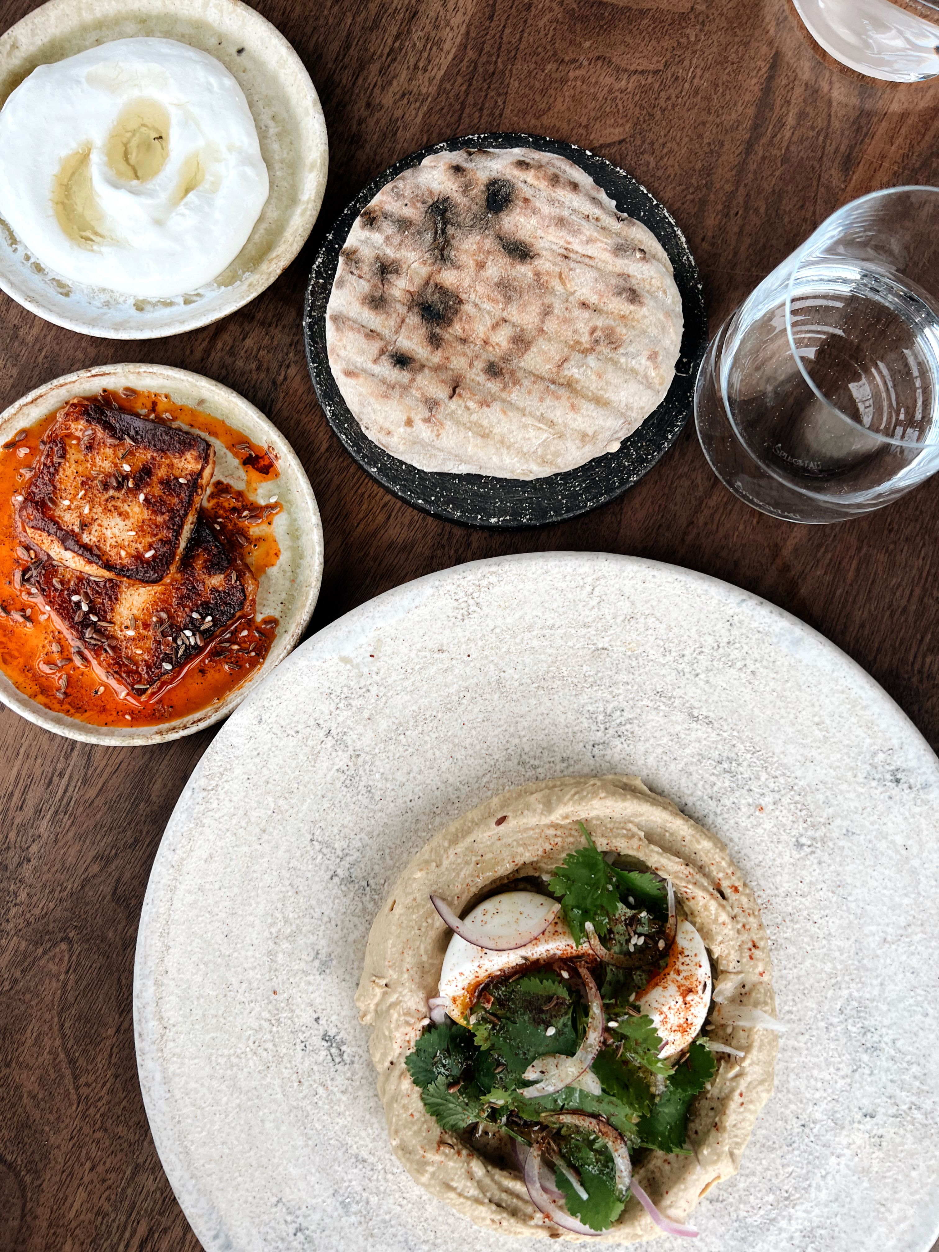 A variety of Mediterranean dishes including hummus and pita served on a wooden table.