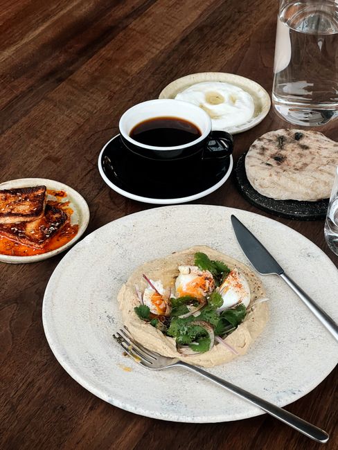 Top view of a rustic brunch with coffee, flatbread, hummus, and grilled halloumi.