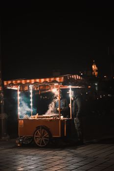 Atmospheric image of a nighttime street vendor selling food at an illuminated cart.