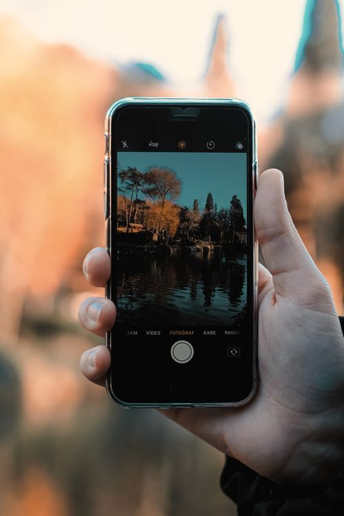 Free A hand holds a smartphone capturing a scenic outdoor landscape in autumn. Stock Photo