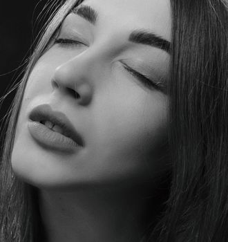 Close-up portrait of a woman with closed eyes in black-and-white, showing elegance and calmness.