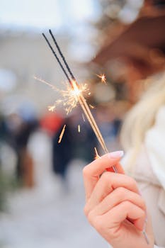 Close-up of a woman's hand holding a lit sparkler outdoors during winter festivity.