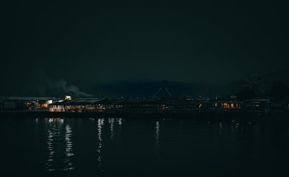 Dark funfair scene with lights reflecting on the seaside at night.