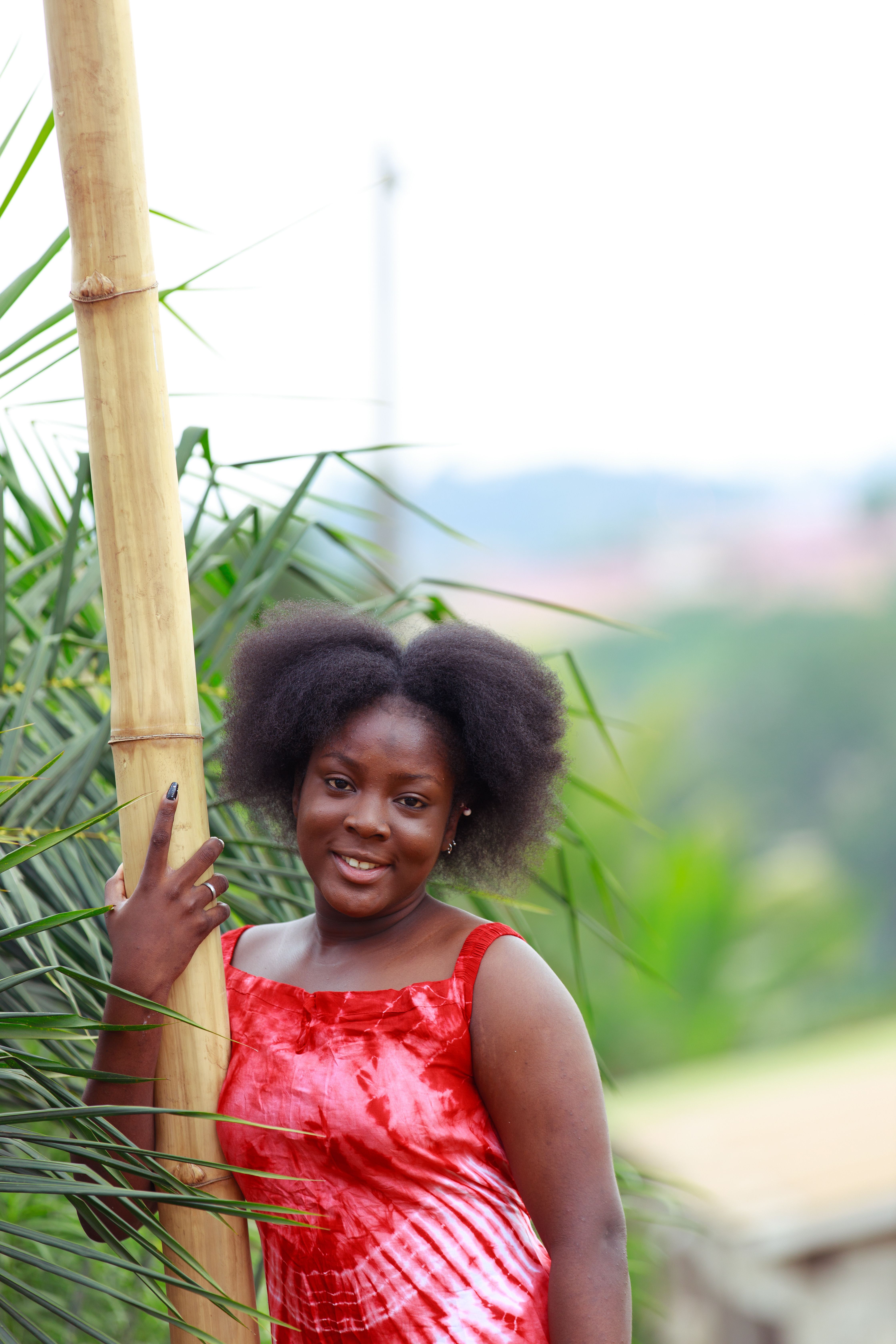 A smiling woman with natural afro hair poses outdoors in a red dress.