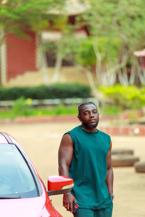 A Man Wearing Black Muscle Shirt Standing Beside Red Car