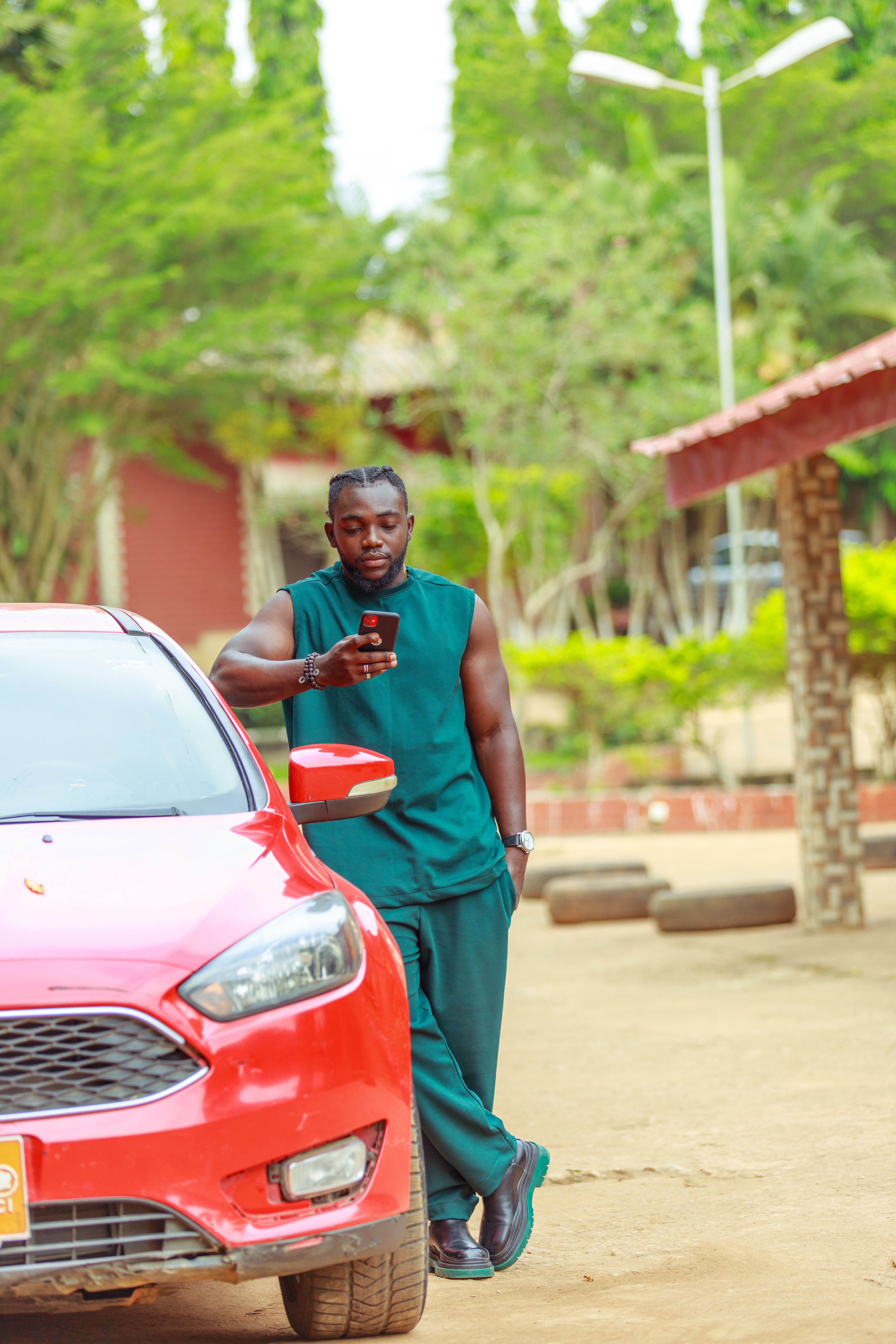Casual man leaning on a red car using smartphone outdoors. Ideal for lifestyle and technology themes.
