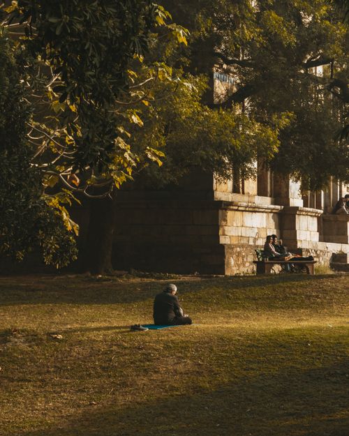 Free A man sits alone in a grassy park near a historic building, basking in the golden hour light. Stock Photo