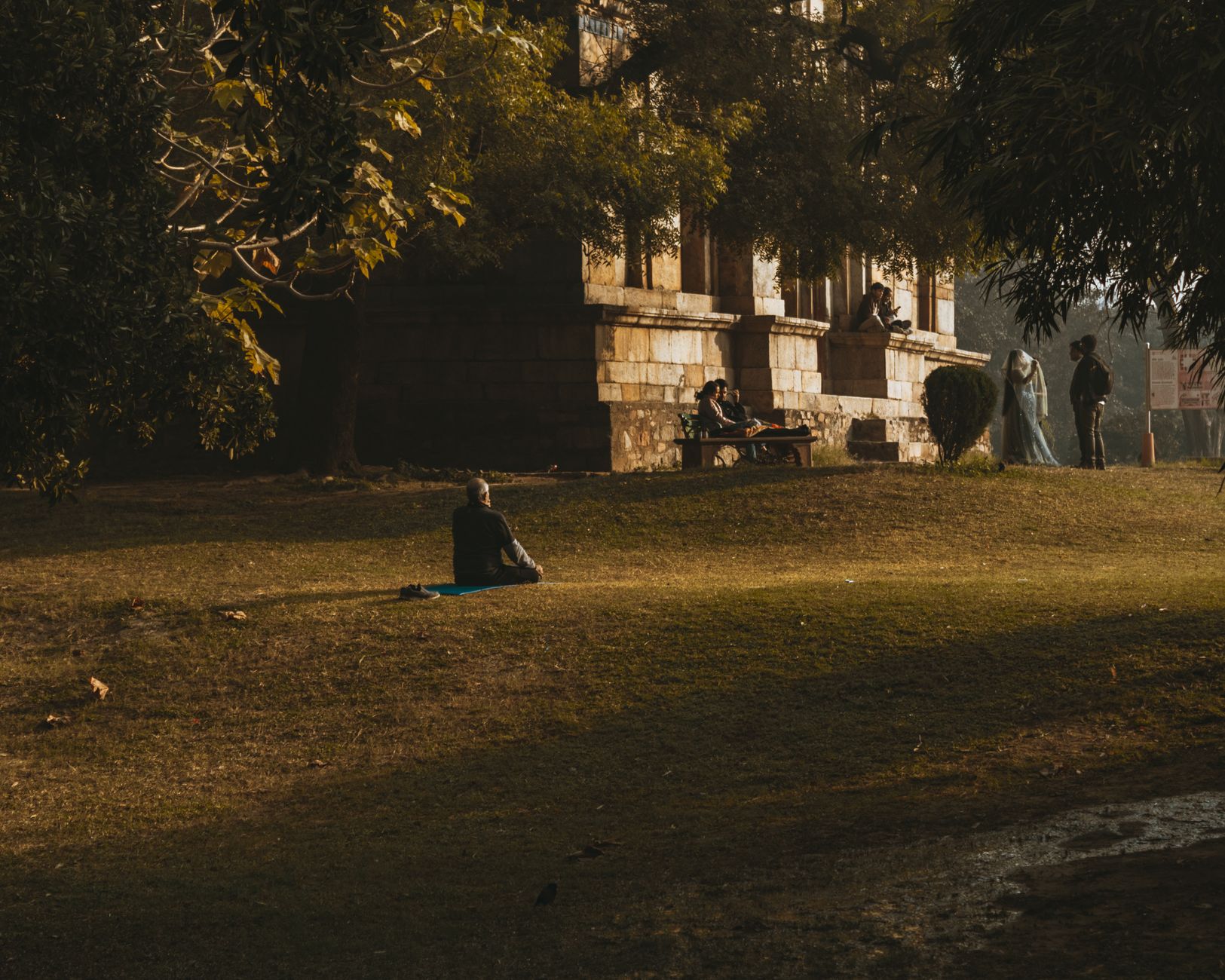 A person meditates on a mat in a tranquil park amidst historical architecture, capturing peace and relaxation.