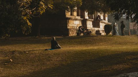A person meditates on a mat in a tranquil park amidst historical architecture, capturing peace and relaxation.