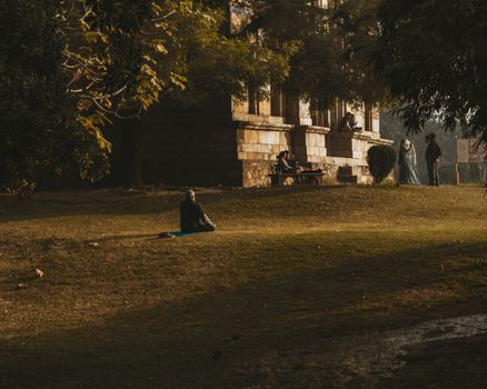 A person meditates on a mat in a tranquil park amidst historical architecture, capturing peace and relaxation.