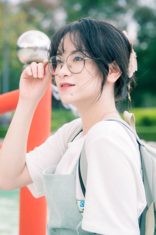 Free A cheerful young woman with glasses enjoys a bright day outdoors, embodying youthful style and positivity. Stock Photo