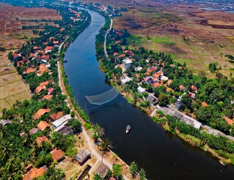 Scenic aerial shot of Muara Gembong, Indonesia, showcasing the river, lush greenery, and village homes.