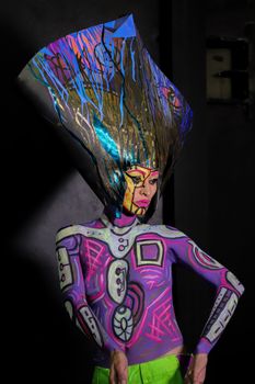 Model with colorful body paint and futuristic headdress posing indoors.