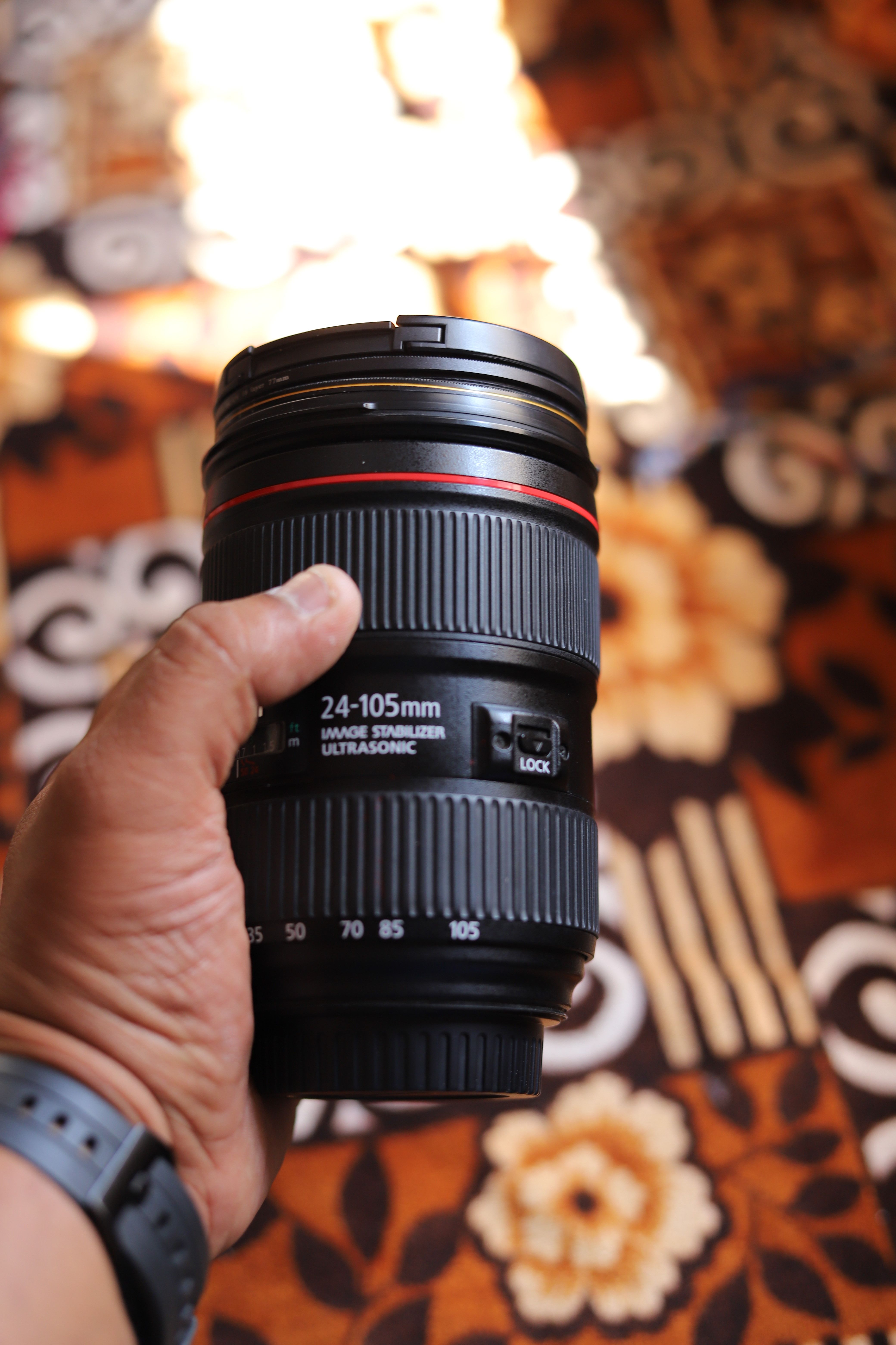 A close-up shot of a Canon lens being held against a patterned background.