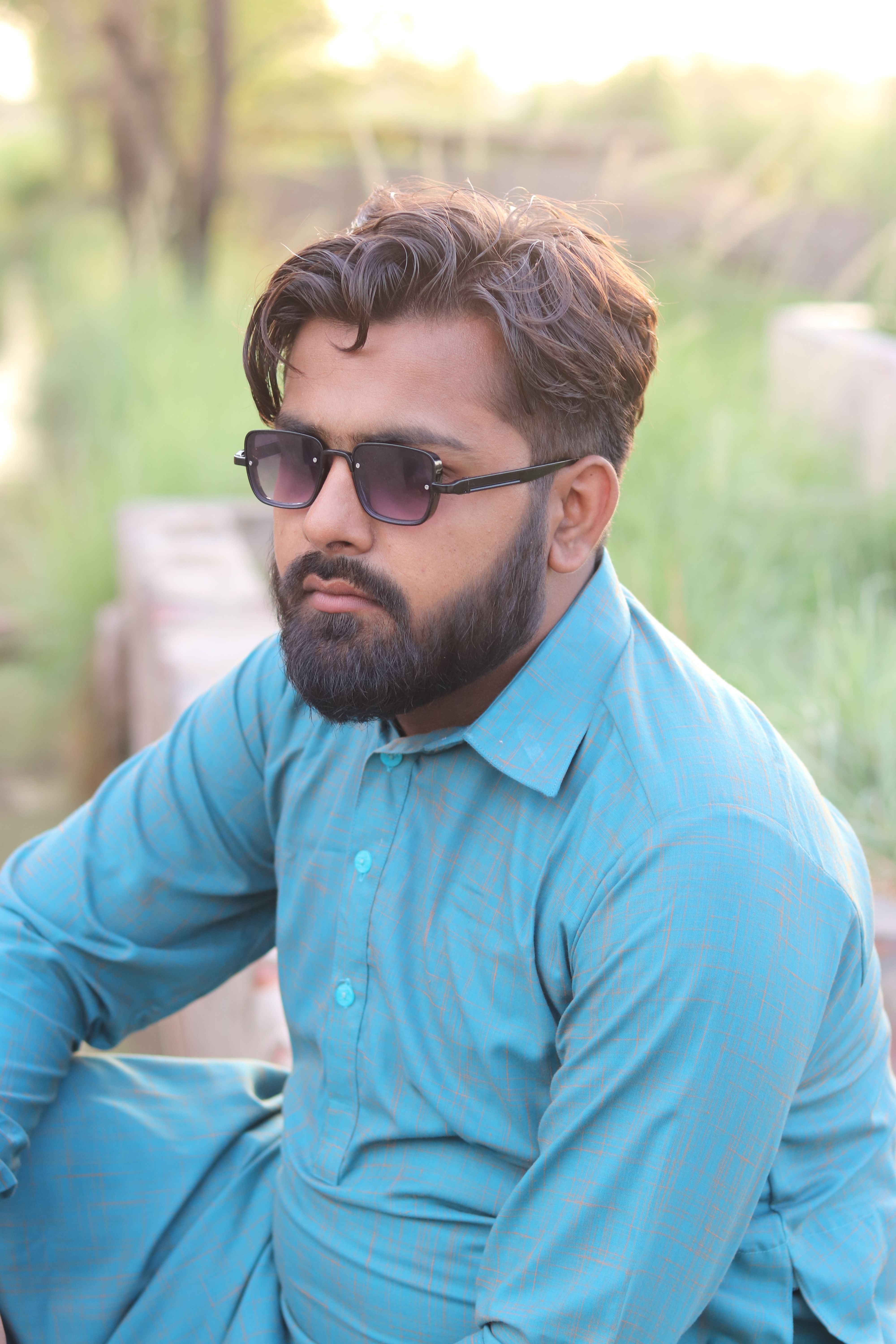 Casual outdoor portrait of a bearded man in sunglasses, wearing a blue shirt.