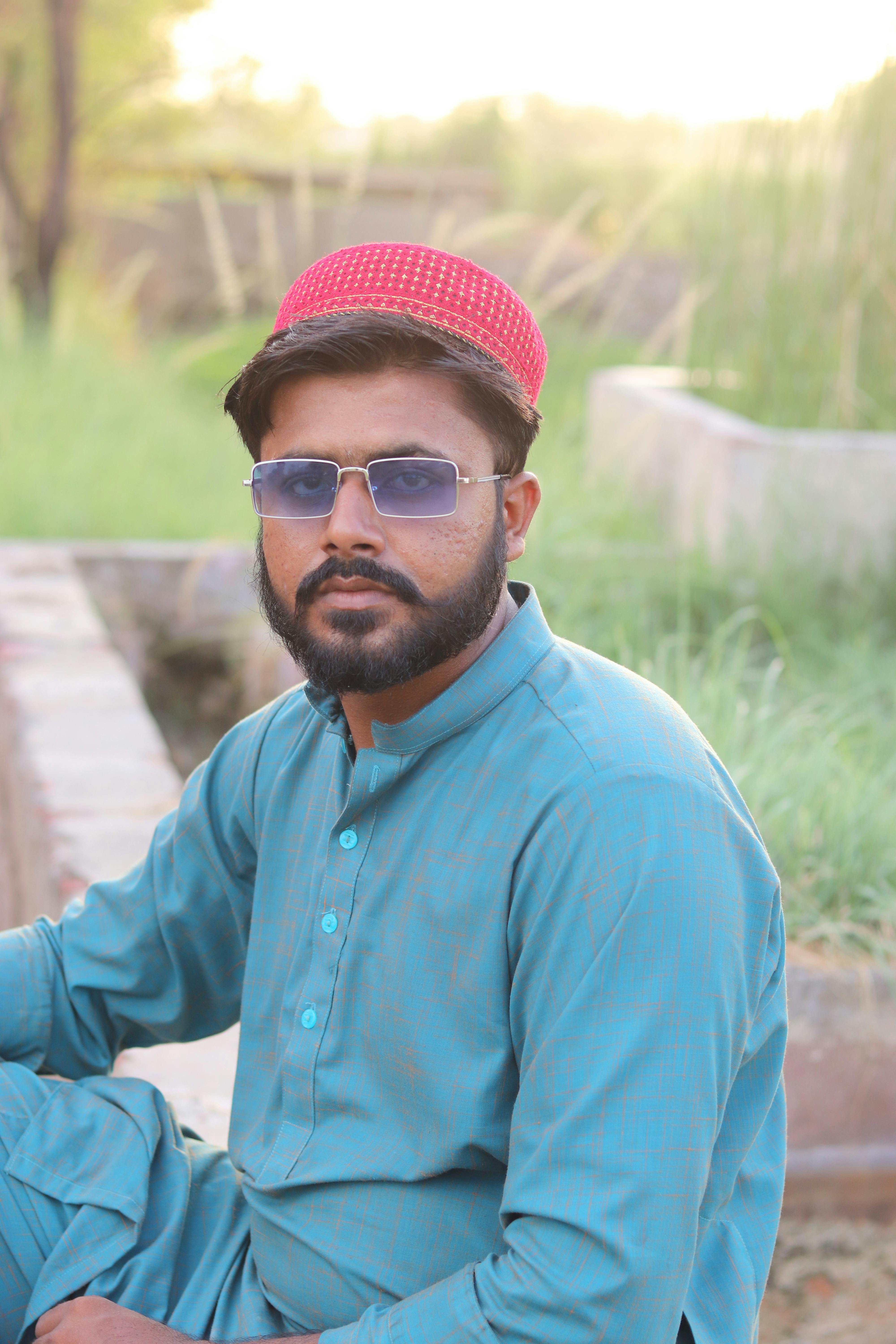 A man in traditional attire and sunglasses sits outdoors, exuding style and cultural essence.
