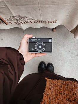 A person's hand holding a vintage AGFA camera from above, showcasing a classic style.
