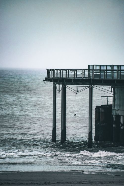 Free An isolated pier extends over a turbulent sea under a grey sky, creating a serene yet moody atmosphere. Stock Photo