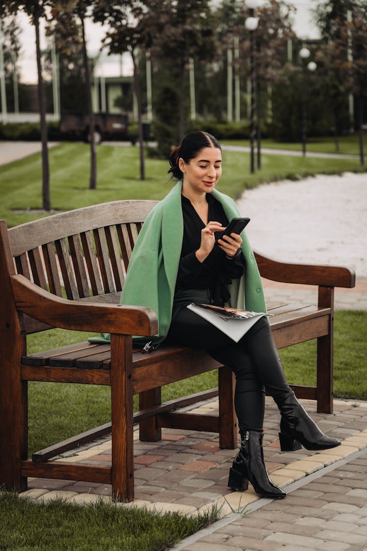 Woman Sitting On A Park Bench Using Her Phone