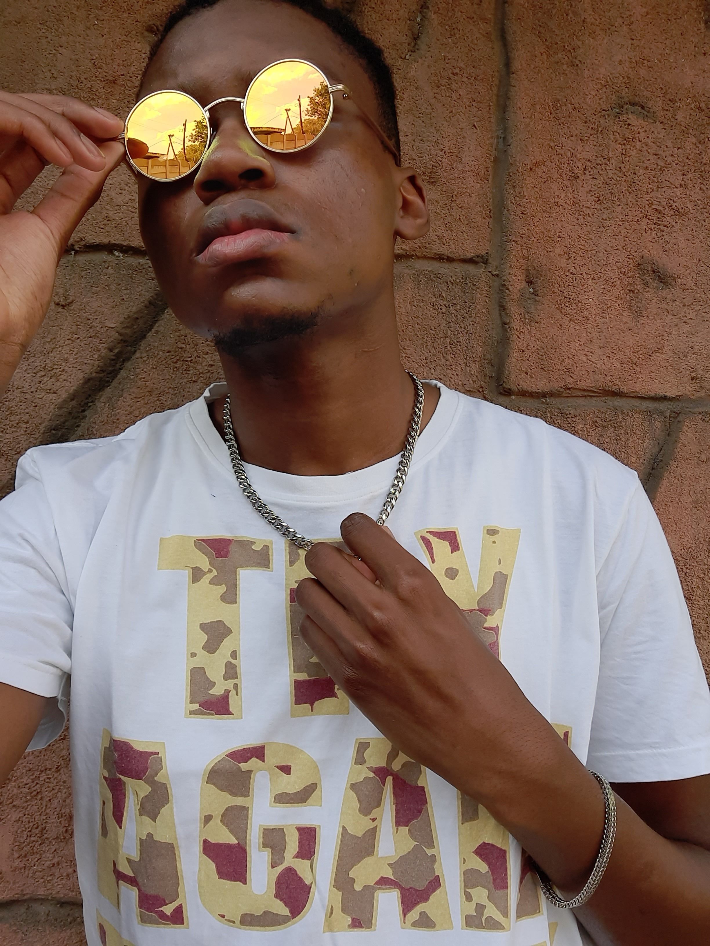Fashionable man in casual t-shirt adjusting reflective sunglasses against a textured wall.